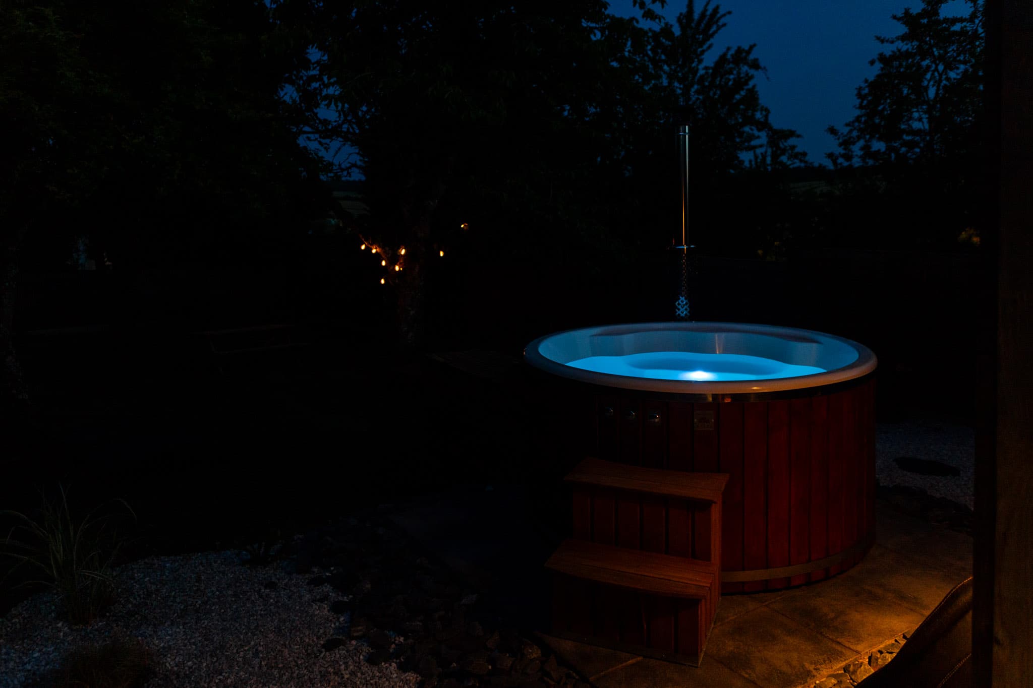Bain nordique illuminé la nuit dans le jardin du gîte
